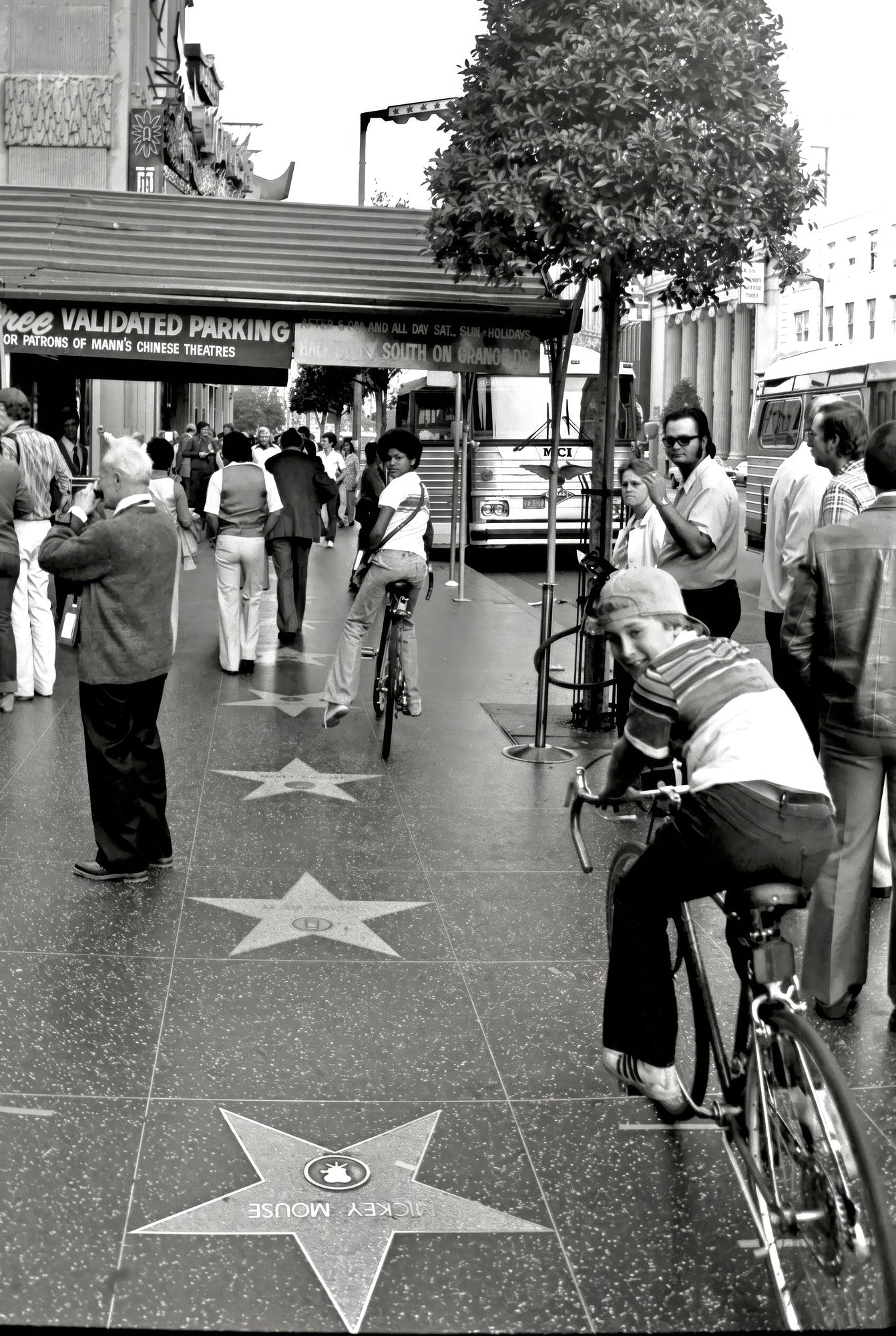 Kids on bikes near the Mickey Mouse star on Hollywood Boulevard's Walk of Fame, Mann's Chinese Theatre awning behind.