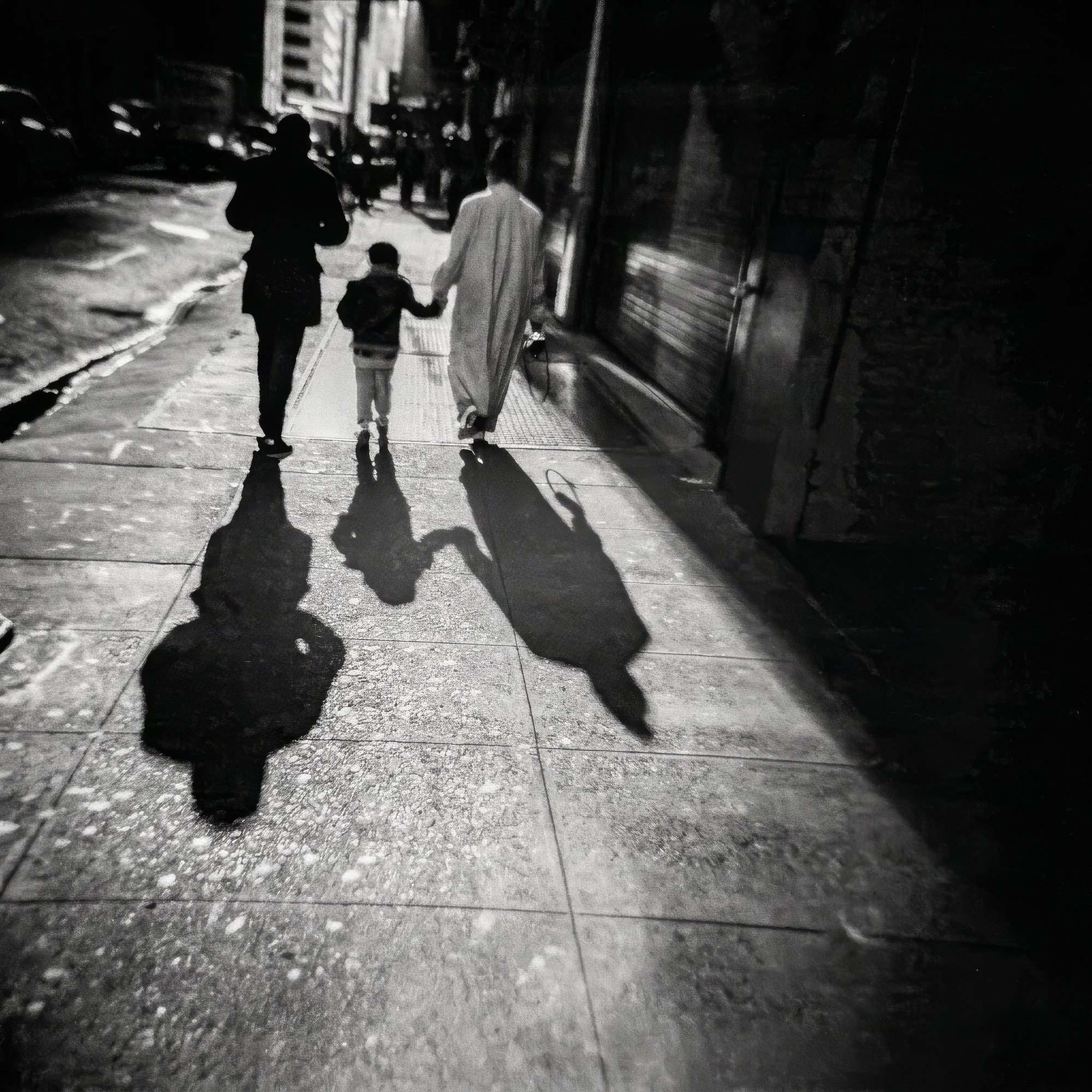Mother, father and child cast long shadows on a city sidewalk at night.